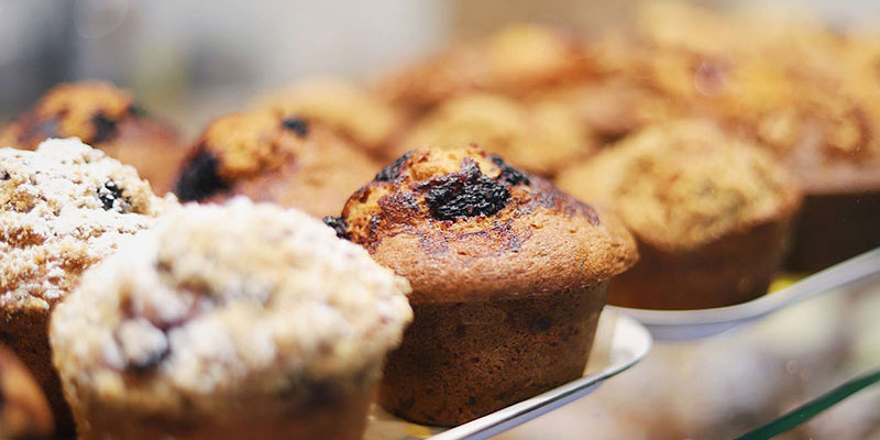 Different flavors of muffins lines up on 2 shelves of trays