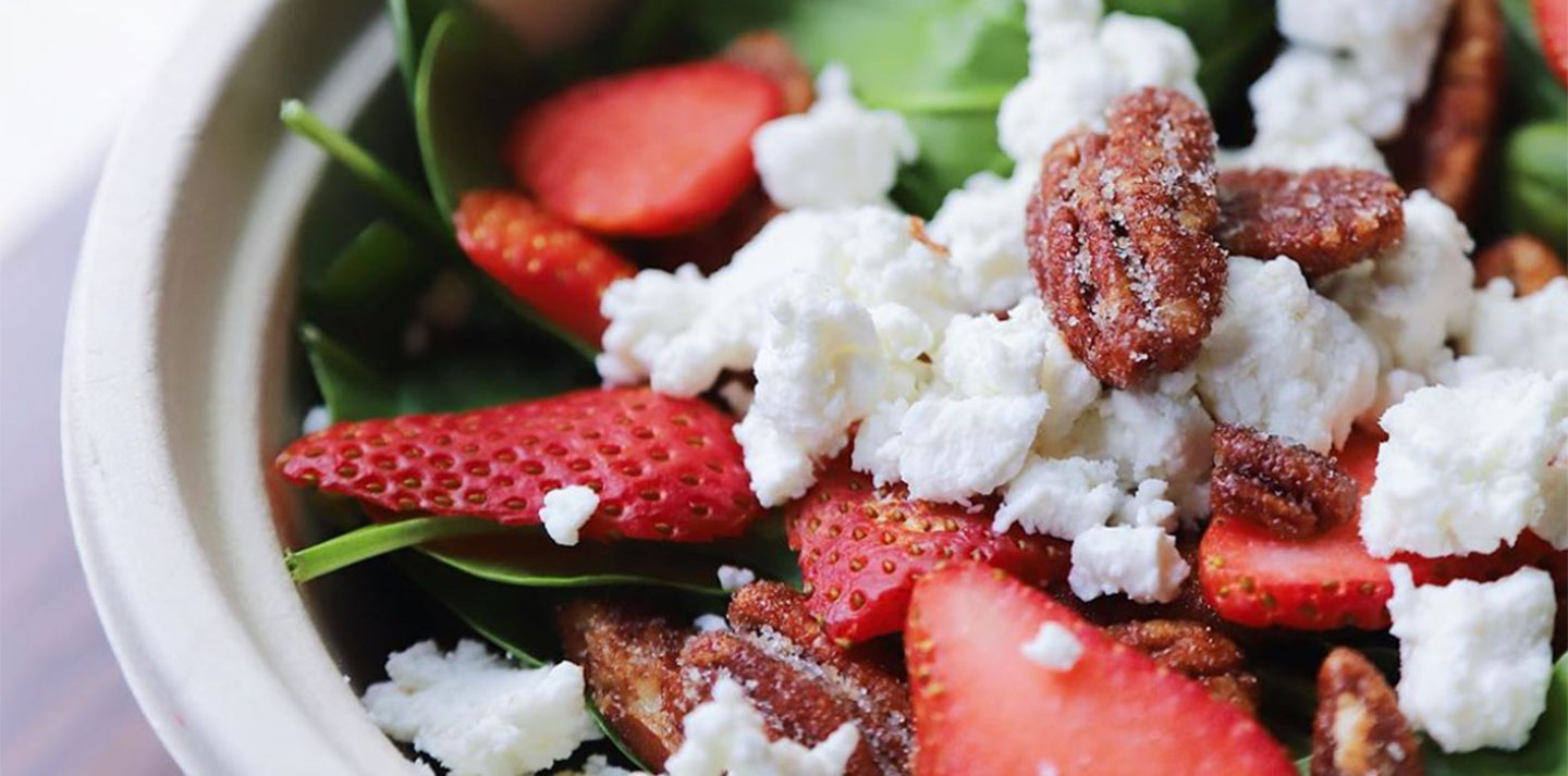 Spinach salad in a bowl with feta cheese, strawberries, and spiced pecans on top.